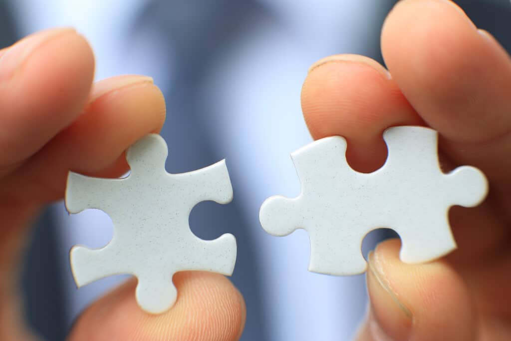 A pair of hands linking two white puzzle pieces that go together.